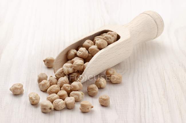 Chick-peas in wooden scoop on wooden surface — Stock Photo
