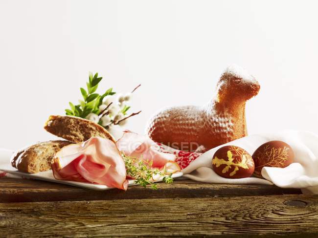 Великодній сніданок з хлібом, шинкою, пофарбованими яйцями та пасхальним ягням на дерев'яній поверхні — стокове фото