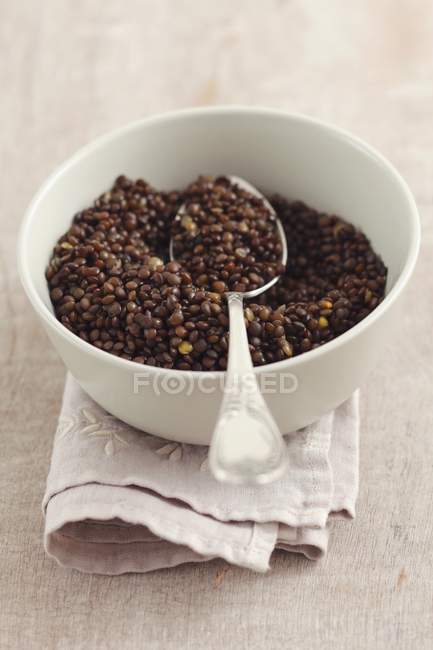 Closeup view of a white bowl of cooked beluga lentils with spoon — Stock Photo