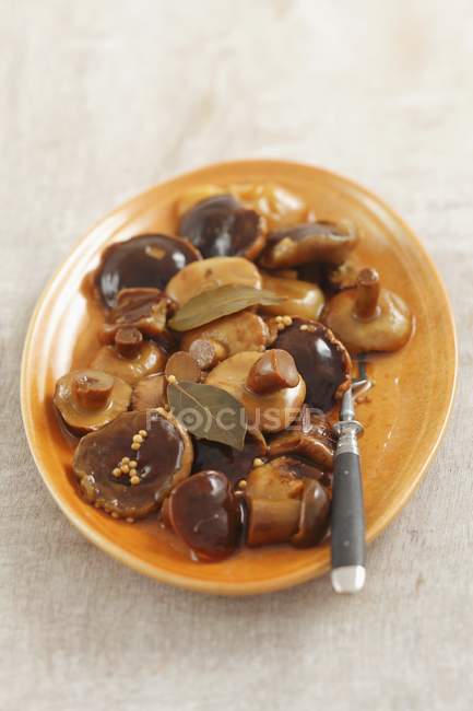 Elevated view of pickled mushrooms with bay leaves and a fork on an orange plate — Stock Photo