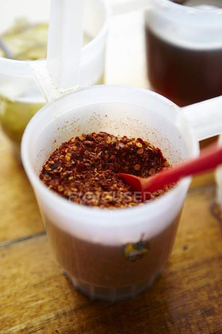 Closeup view of Chilli flakes with red spoon in plastic cup — Stock Photo