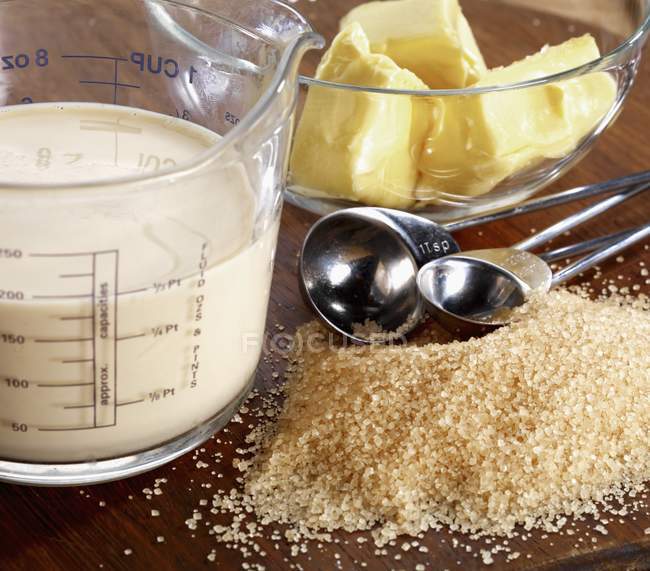 Closeup view of brown sugar heap with milk in measuring dish and butter in glass bowl — Stock Photo