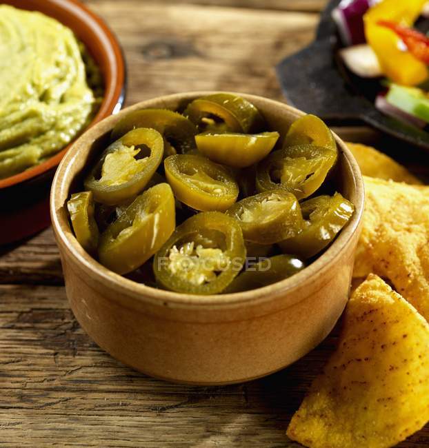 Eingelegte Jalapeos, Guacamole und Tortilla-Chips in brauner Schüssel über Holzoberfläche — Stockfoto
