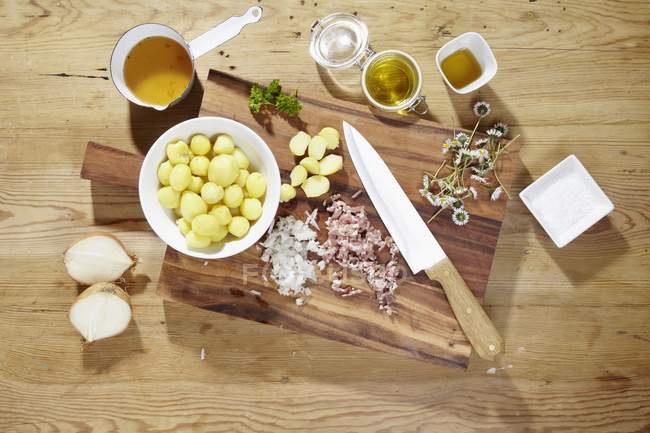 Ингредиенты для приготовления картофельного салата с маргаритками на деревянной поверхности с письменным столом и ножом — стоковое фото