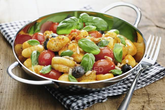Gnocchi mit Tomaten, Oliven, Pinienkernen und Basilikum im Wok über Handtuch — Stockfoto