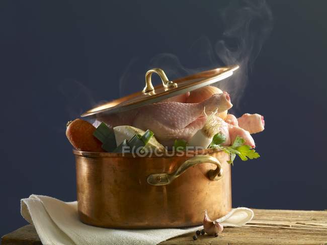 Тушкована курка з овочами в мідному горщику над дерев'яною поверхнею з рушником — стокове фото
