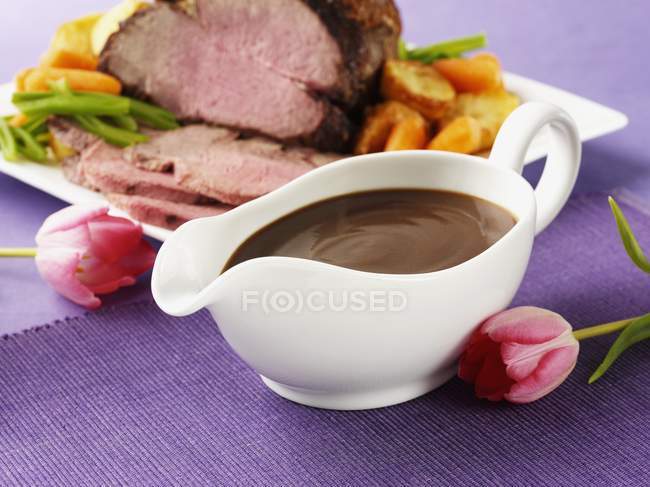 Closeup view of creamy gravy with meat and vegetable dish by flowers — Stock Photo