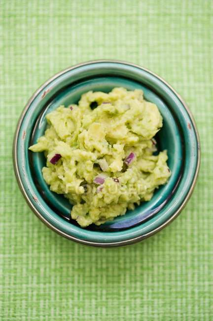 Guacamole con cipolle sul piatto su superficie verde — Foto stock