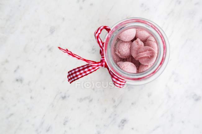 Gros plan vue du dessus des bonbons de framboises dans un bocal sur une surface de marbre — Photo de stock