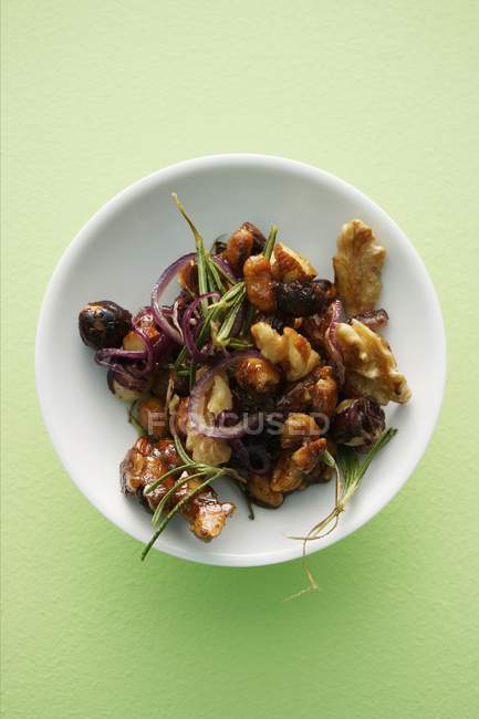Roasted nuts with rosemary and shallots on white plate  over green surface — Stock Photo