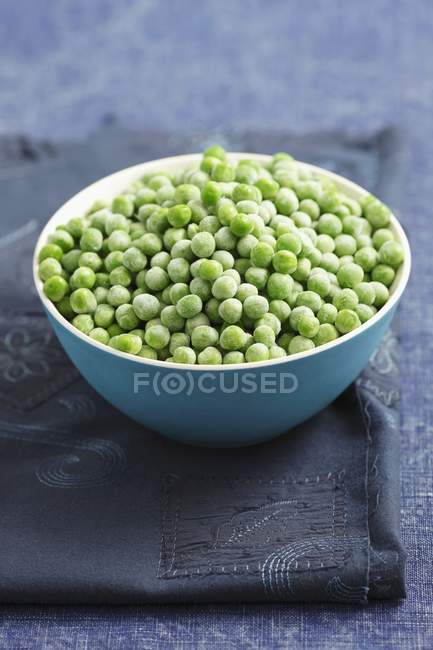 Frozen peas in a blue  bowl over black towle on table — Stock Photo