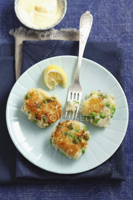 Pasteles de pescado con guisantes en plato - foto de stock
