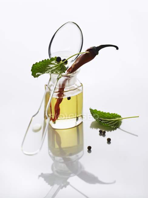 Öl, Kräuter, eine Chilischote und Pfefferkörner auf weißem Hintergrund — Stockfoto