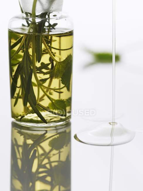 Óleo de ervas em uma garrafa e fluindo em uma superfície reflexiva — Fotografia de Stock