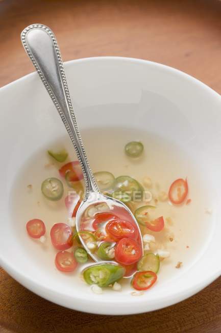 Spicy chilli sauce in bowl with spoon over wooden surface — Stock Photo