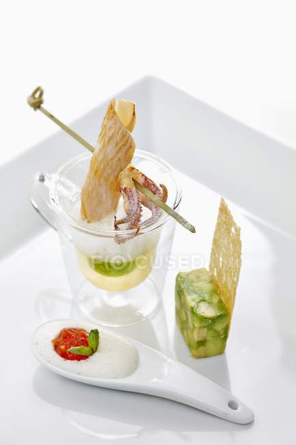 Avocado soup with an octopus skewer and asparagus terrine in white dish over white surface — Stock Photo