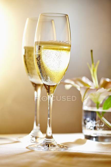 Glasses of champagne in front of a vase of flowers — Stock Photo