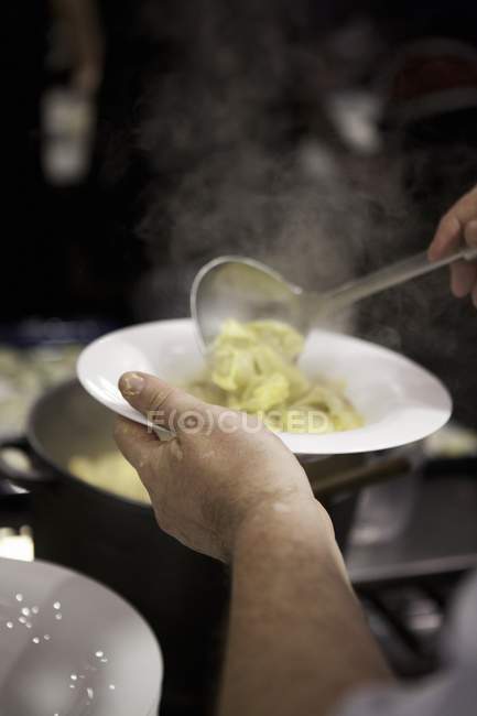 Chef cucharada tortellini en la placa - foto de stock
