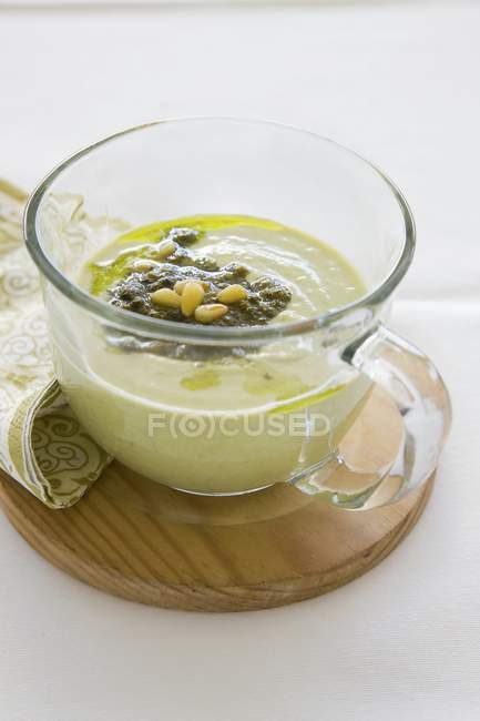 Cream of asparagus with pesto and pine nuts in glass over wooden desk — Stock Photo