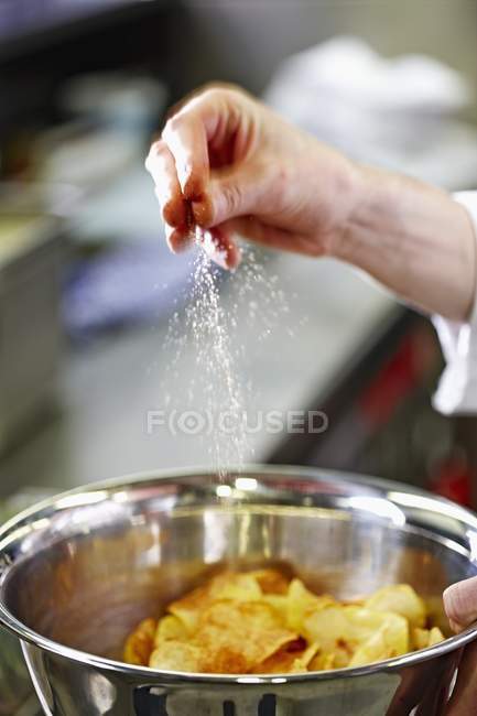 Menschliche Hand beim Salzen von Kartoffelchips — Stockfoto