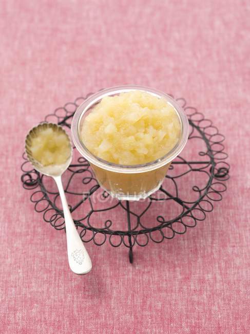 A bowl of apple sauce on a pot holder over pink surface — Stock Photo