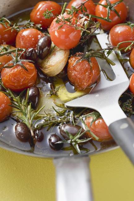 Fried cherry tomatoes with garlic and olives in frying pan — Stock Photo