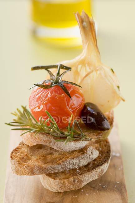 Fried cherry tomato, olive and garlic on toast over wooden desk — Stock Photo
