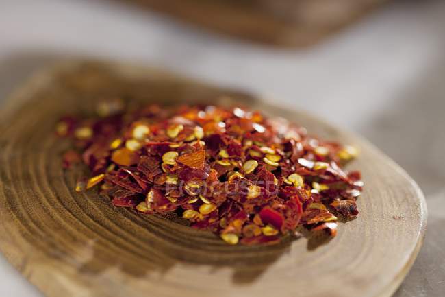 A pile of chilli flakes on a wooden plate — Stock Photo