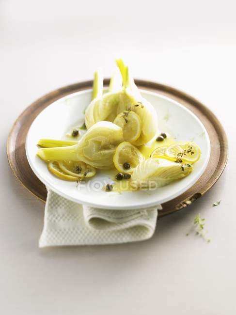Finocchio con salsa di limone e capperi in piatto bianco su vassoio su sfondo bianco — Foto stock