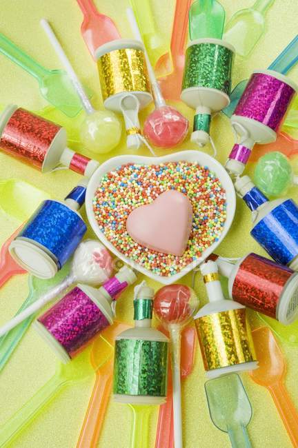 Vista superior del plato en forma de corazón con un corazón de chocolate rosa y poppers de fiesta de colores y cucharas de plástico - foto de stock