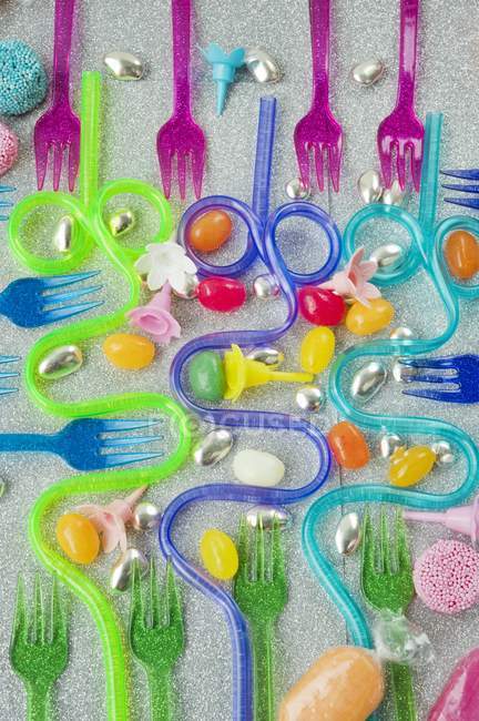Panoramica grafica di forchette da festa in plastica colorata con cannucce da bere curve blu e viola su sfondo argento scintillante con dolci — Foto stock
