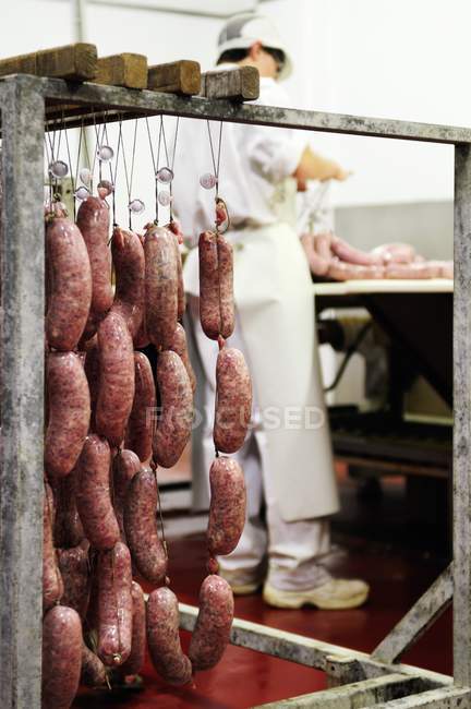 Embutidos italianos frescos colgados en un carnicero con una persona en el fondo - foto de stock