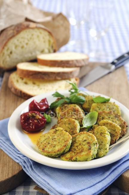 Zucchini-Krapfen mit Basilikum und Brot auf weißem Teller über dem Tisch — Stockfoto