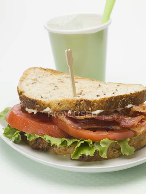 Сэндвич с беконом, салатом и помидорами, напиток на заднем плане — стоковое фото