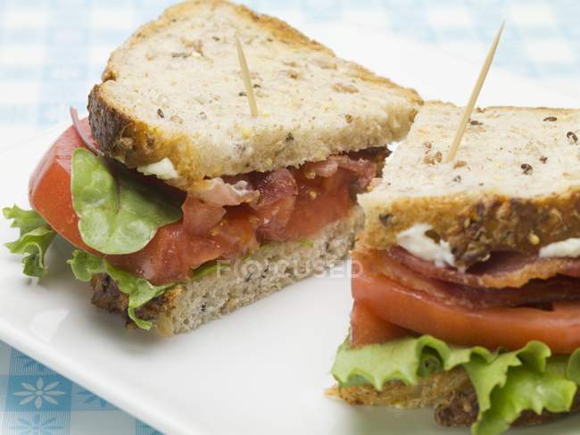 Sandwich au bacon, à la laitue et à la tomate, coupé en deux sur plaque blanche — Photo de stock