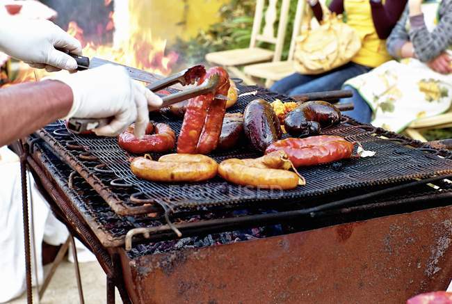 Cropped daytime view of hand arranging various sausages on a rustic barbecue — Stock Photo