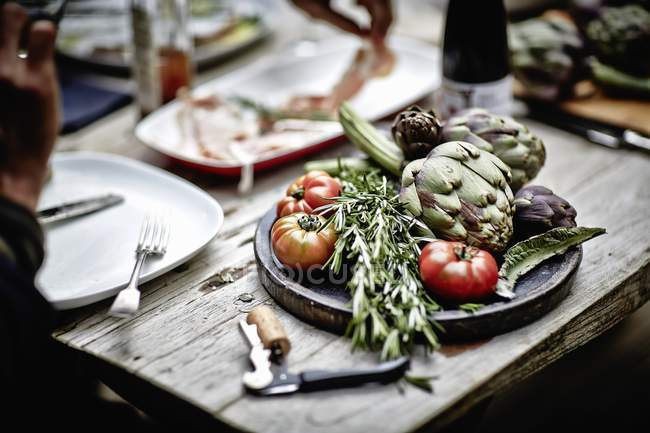 Alcachofas con romero y tomates a bordo - foto de stock
