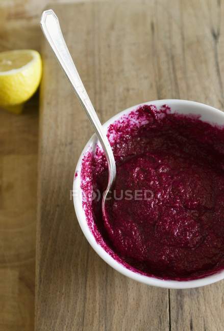 A bowl of beetroot dip with a spoon over wooden surface — Stock Photo