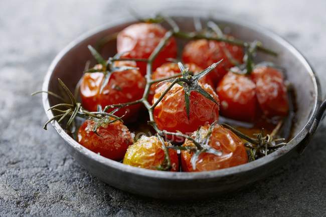 Roasted tomatoes with rosemary on black plate — Stock Photo