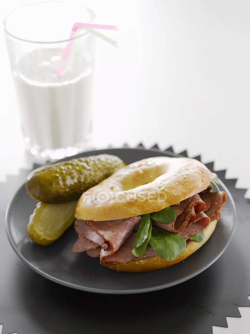 A pastrami and gherkin bagel on black plate — Stock Photo