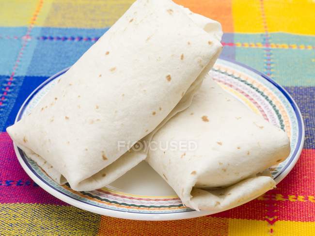 Closeup view of two tortilla parcels on plate and colorful cloth — Stock Photo