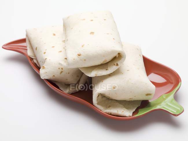 Tortilla parcels in chilli pepper shaped dish on white background — Stock Photo