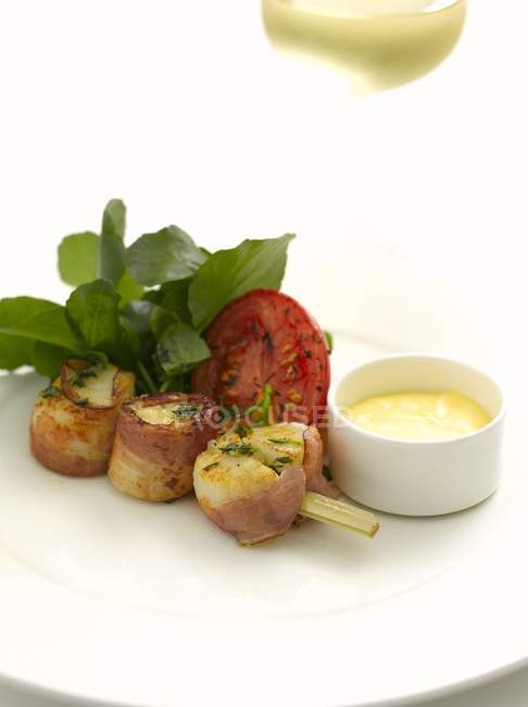 Closeup view of scallops in bacon on skewer with tomato half, herbs and sauce — Stock Photo