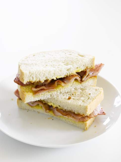 Um sanduíche de bacon na placa branca sobre fundo branco — Fotografia de Stock