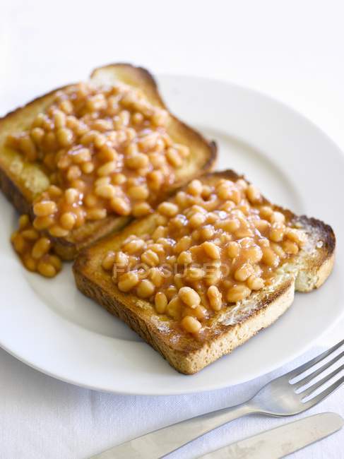 Baked beans on toast over white plate with fork and knife — Stock Photo
