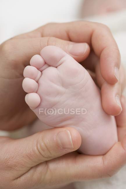 Vista de cerca de las manos sosteniendo un pie de bebé - foto de stock