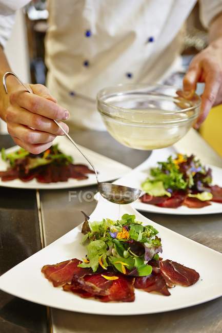 Cropped view of chef drizzling dressing on salad — Stock Photo