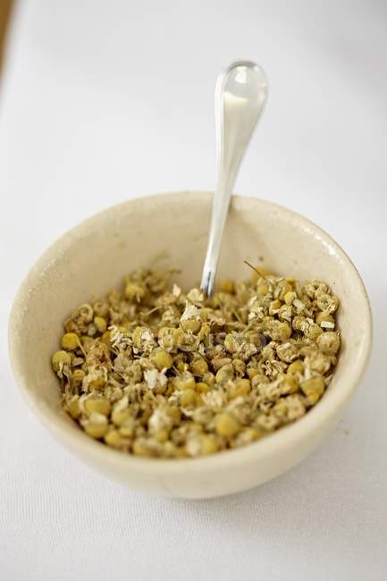 Closeup view of dried camomile flowers in a bowl with a spoon — Stock Photo