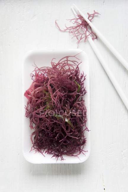 Вид зверху на білу миску з червоних водоростей з паличками — стокове фото