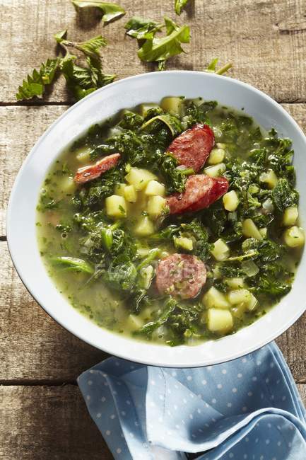 Heggenms stew made with wild herbs, green kale and sausages  on white plate over wooden surface — Stock Photo
